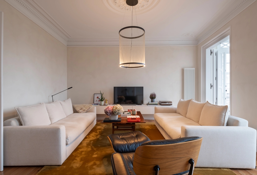 Vista panorámica de salón con dos sofás blancos enfrentados sobre alfombra mostaza.