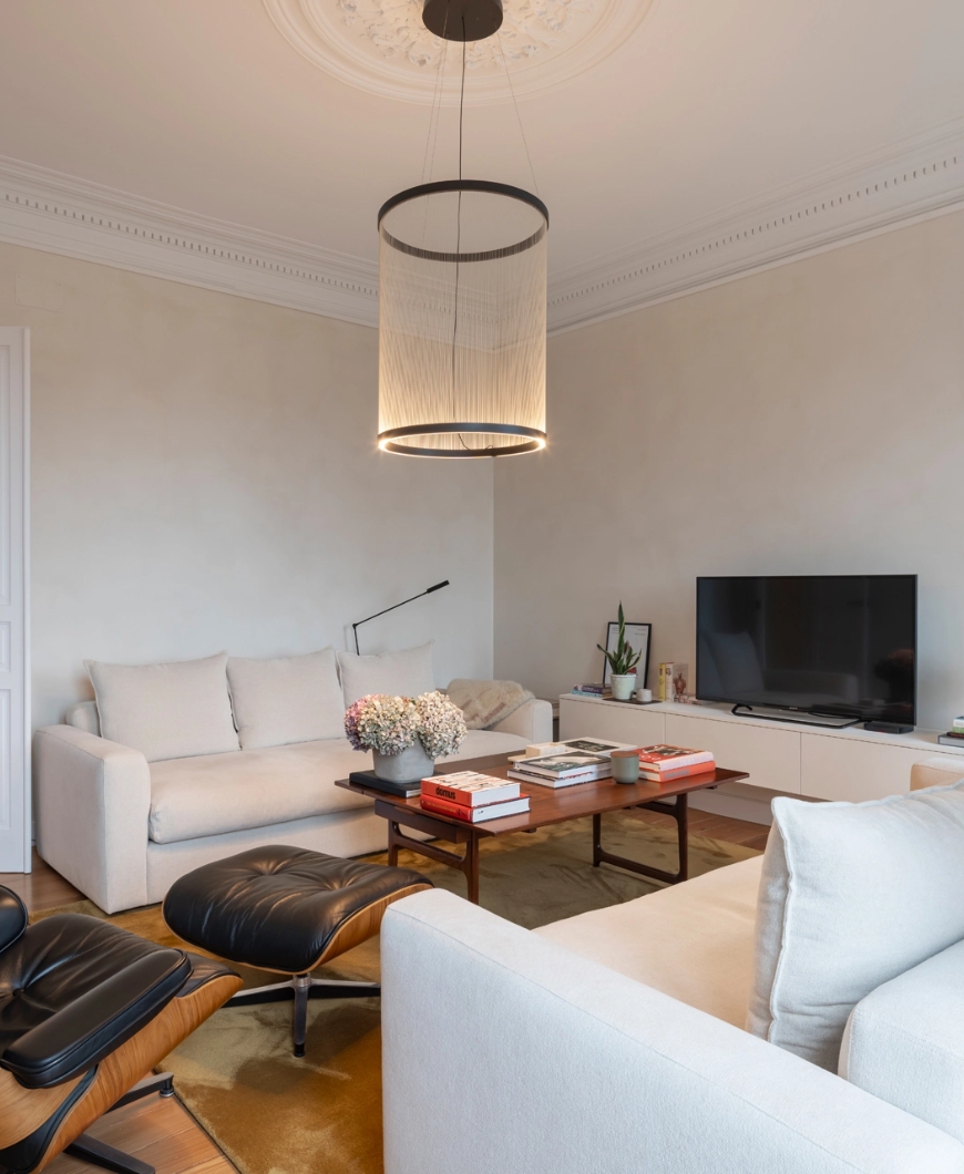 Salón moderno con sofás blancos, mesa de centro de madera y lámpara cilíndrica.