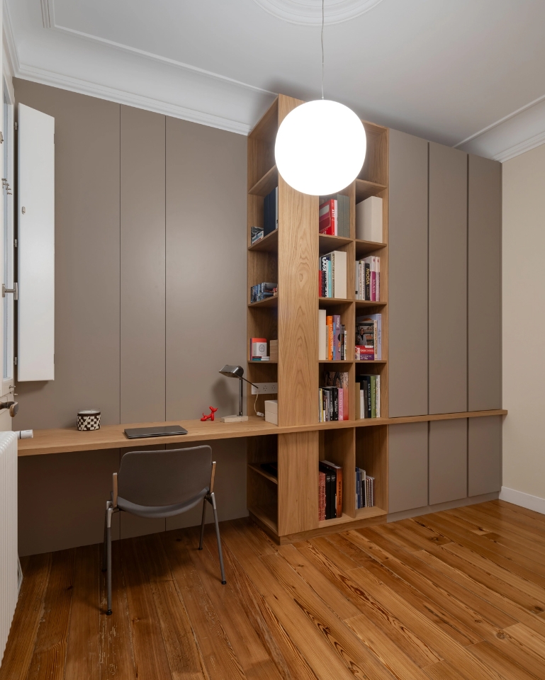 Zona de estudio con escritorio de madera, estantería integrada y armarios color visón.