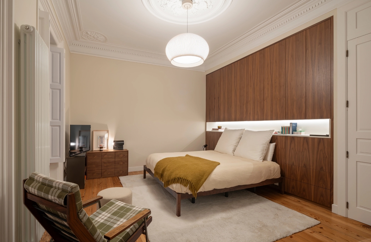 Dormitorio principal con armario de madera empotrado, butaca de cuadros y lámpara globo.