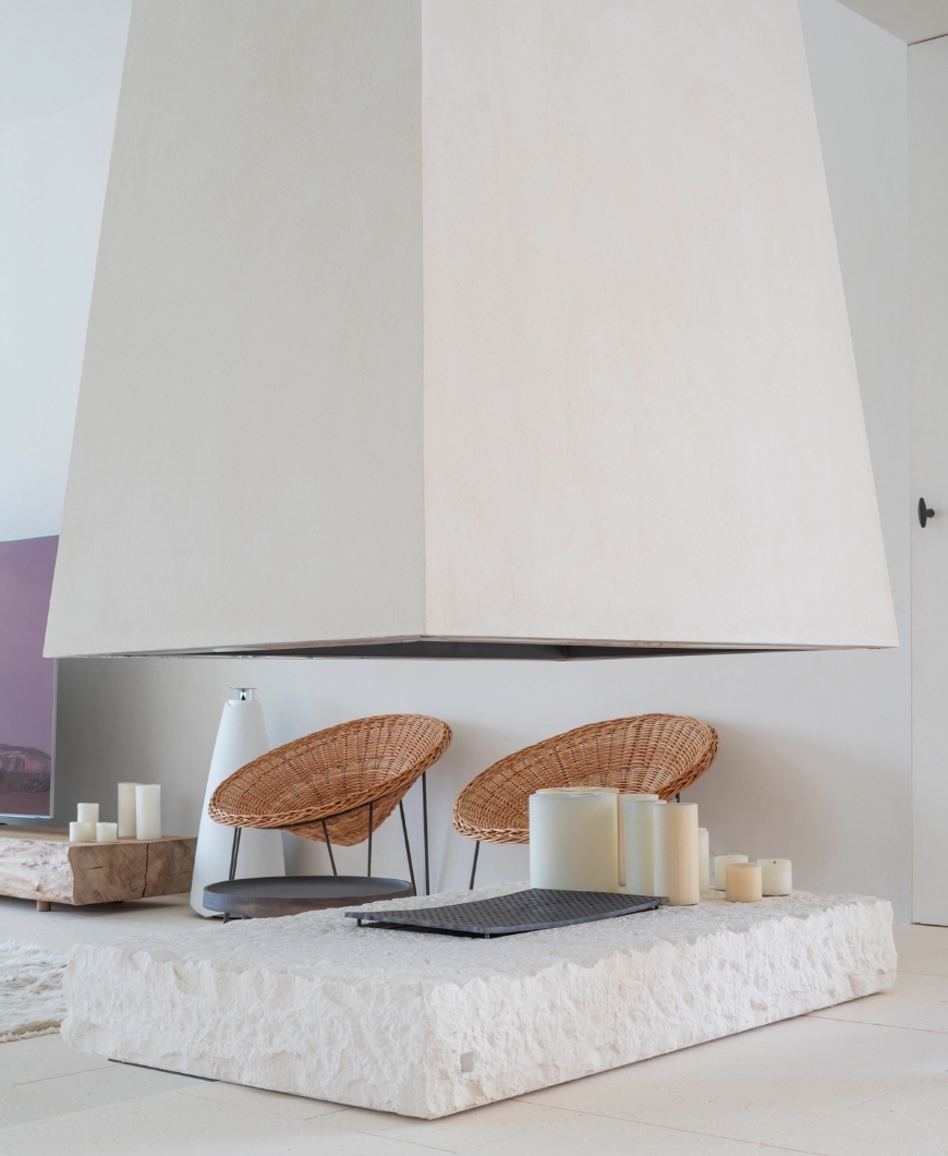 Minimalist fireplace suspended on a stone base with wicker armchairs and decorative candles.