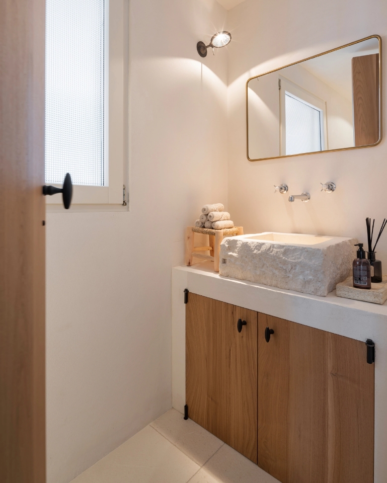 Toilet with carved natural stone washbasin, gilt-framed mirror and vanity unit with wooden doors.