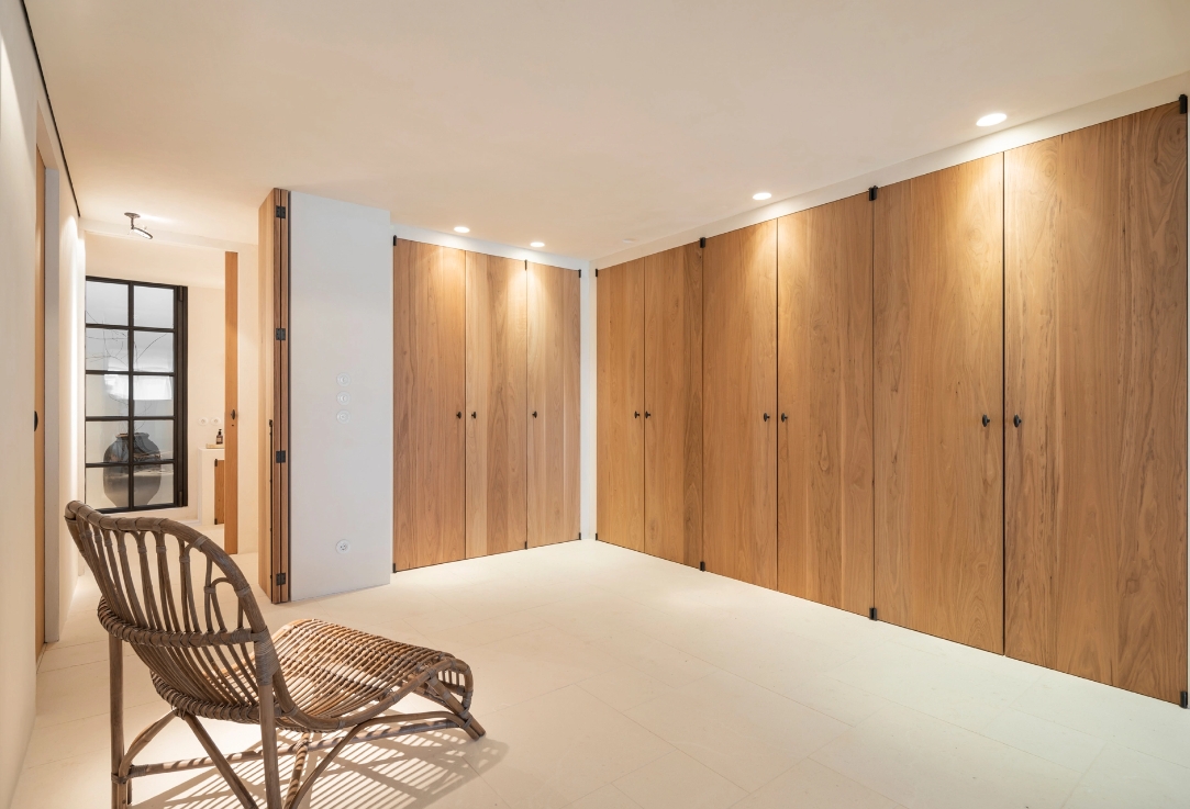 Floor-to-ceiling wooden built-in closets in minimalist room with wicker chair.