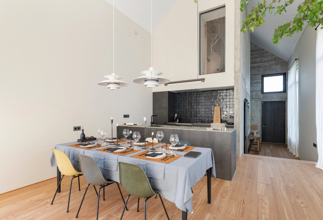 Dining room with dressed table, colorful chairs and designer lamps in front of open kitchen.