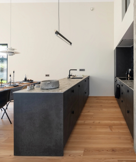 Minimalist kitchen island in dark gray with black sink under suspended linear lamp.