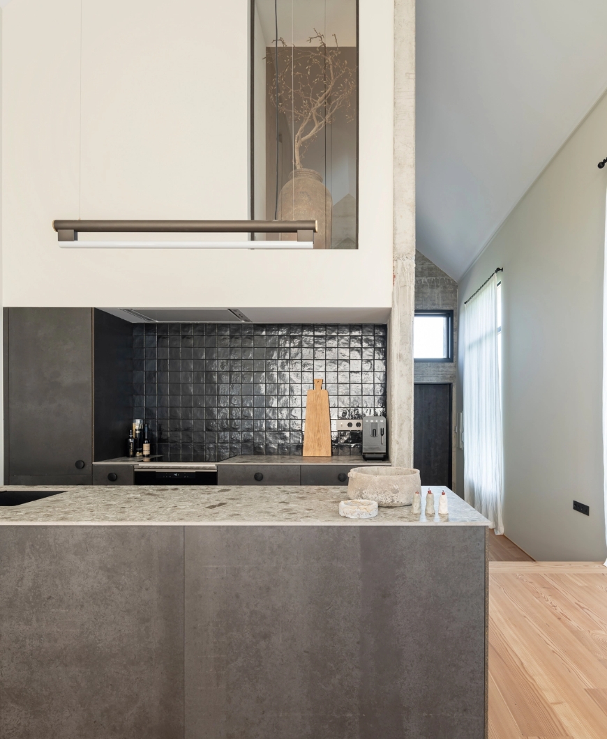 Modern kitchen with dark gray island, stone countertop and glossy black tile front.