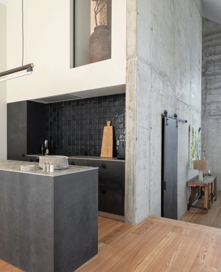 Detail of industrial kitchen with concrete wall, gray island and black tile front.