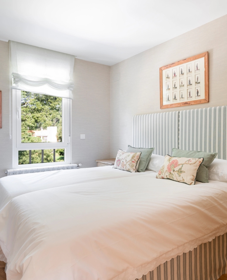 Bright bedroom with green striped headboard, floral cushions and window overlooking trees.