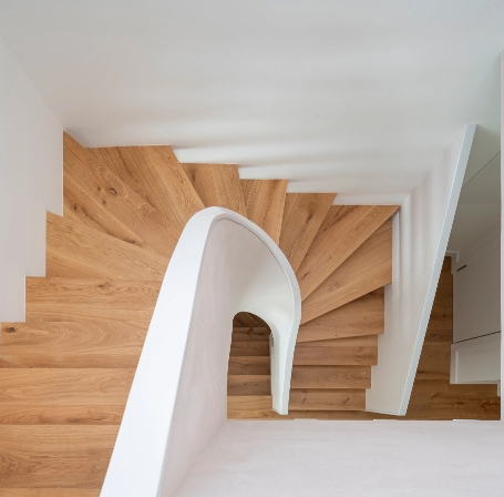 Zenithal view of wooden spiral staircase with white handrail and helical design.