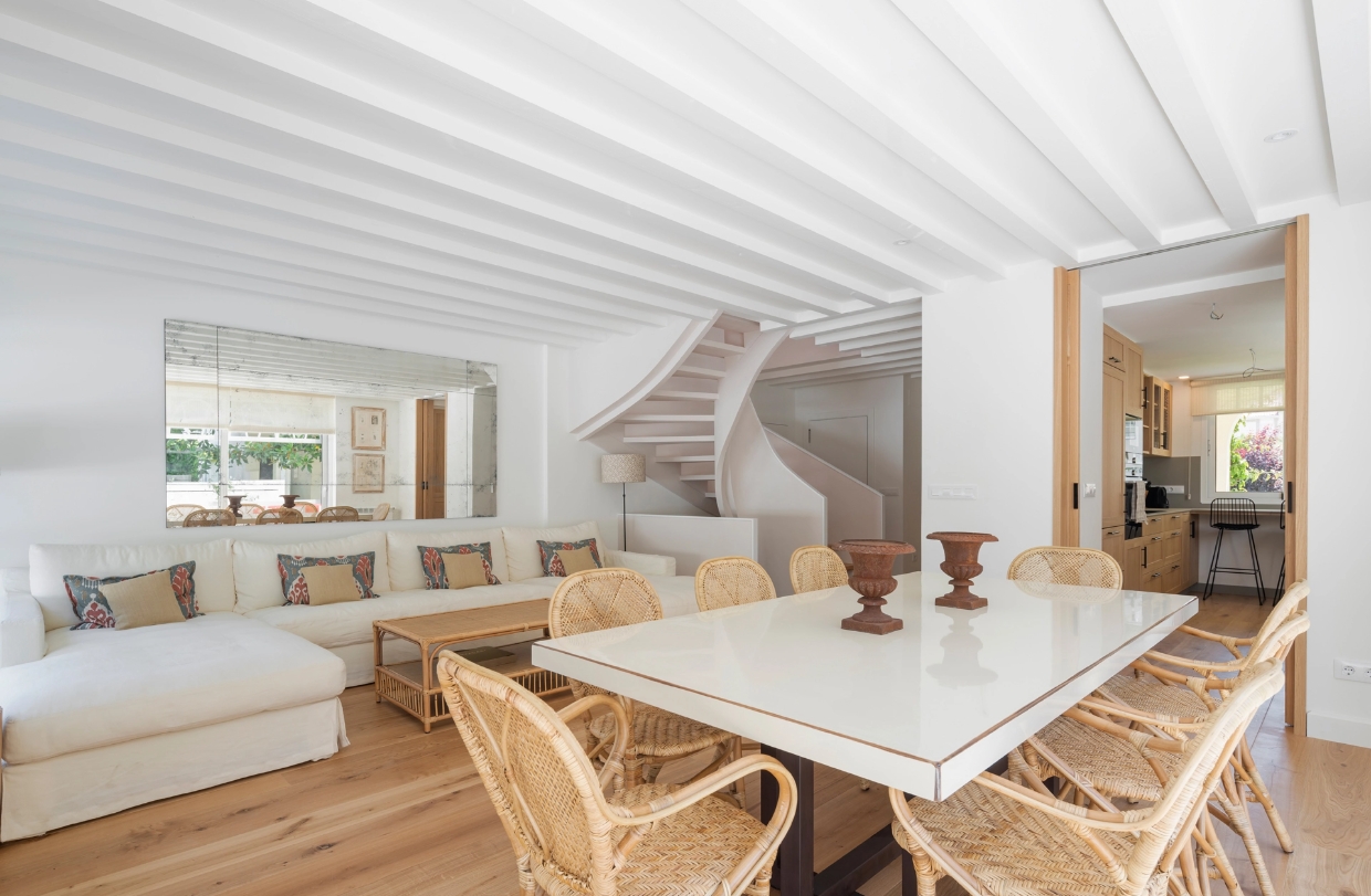 Integrated dining room and living room with white beamed ceiling, spiral staircase and access to the kitchen.