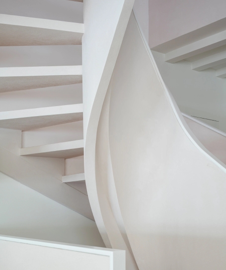 Detail of white spiral staircase with light wood treads and minimalist curved design.