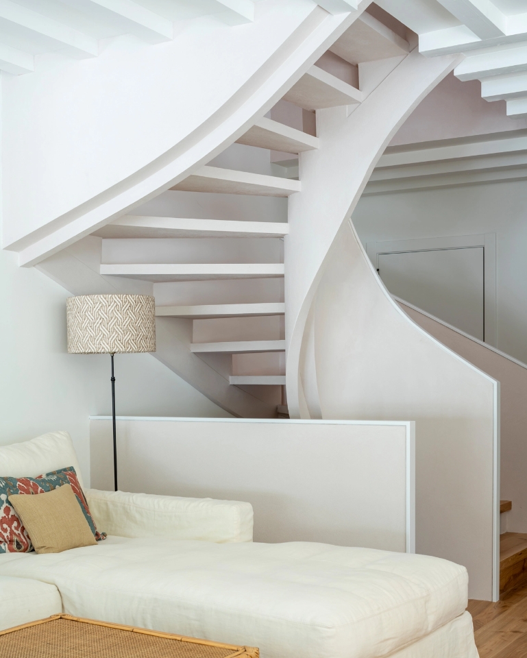 White spiral staircase integrated behind modern living room sofa with floor lamp and ceiling beams.