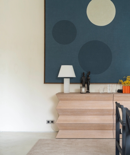 Wooden sideboard with zigzag design under blue square with circles and white table lamp.