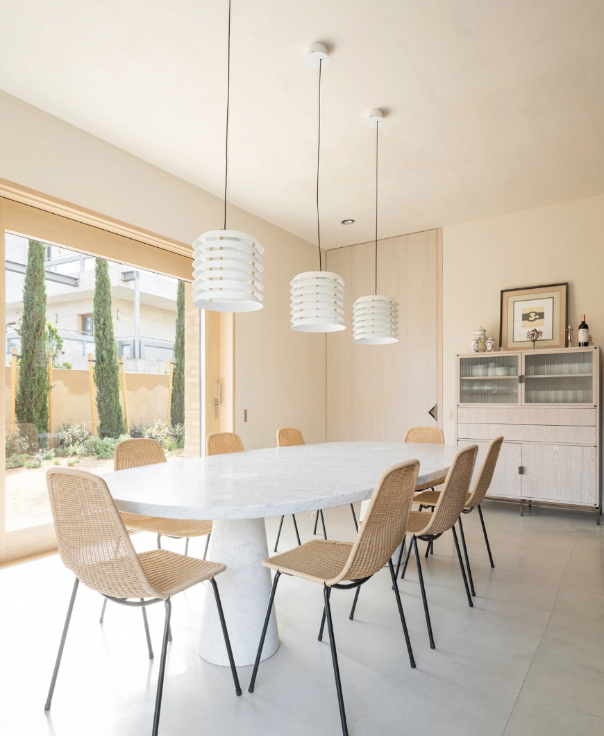 Bright dining room with oval table, wicker chairs and three white designer lamps.