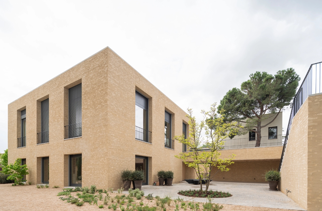 Facade of a modern light brick house with large windows and an interior courtyard with a tree.