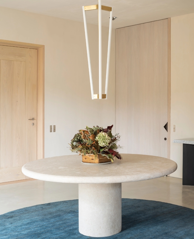 Entrance hall with round stone table on blue carpet and geometric pendant lamp.