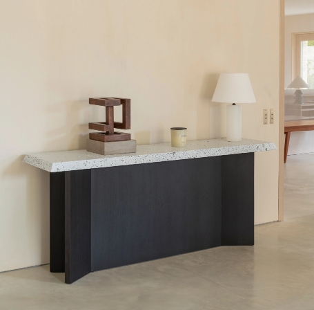 Black design console with terrazzo top, wood sculpture and white lamp on beige wall.