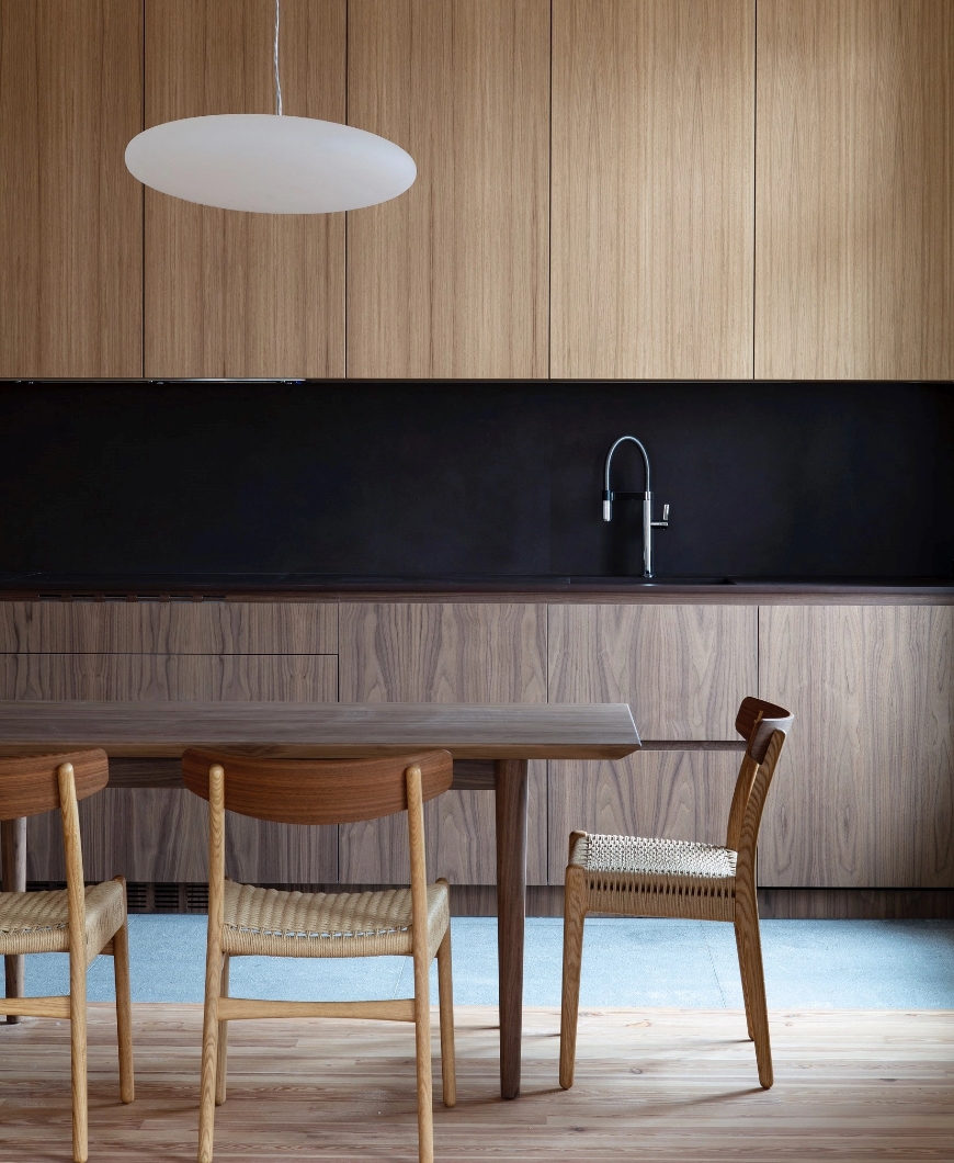 Minimalist kitchen with wooden furniture, black countertop wall and dining table.
