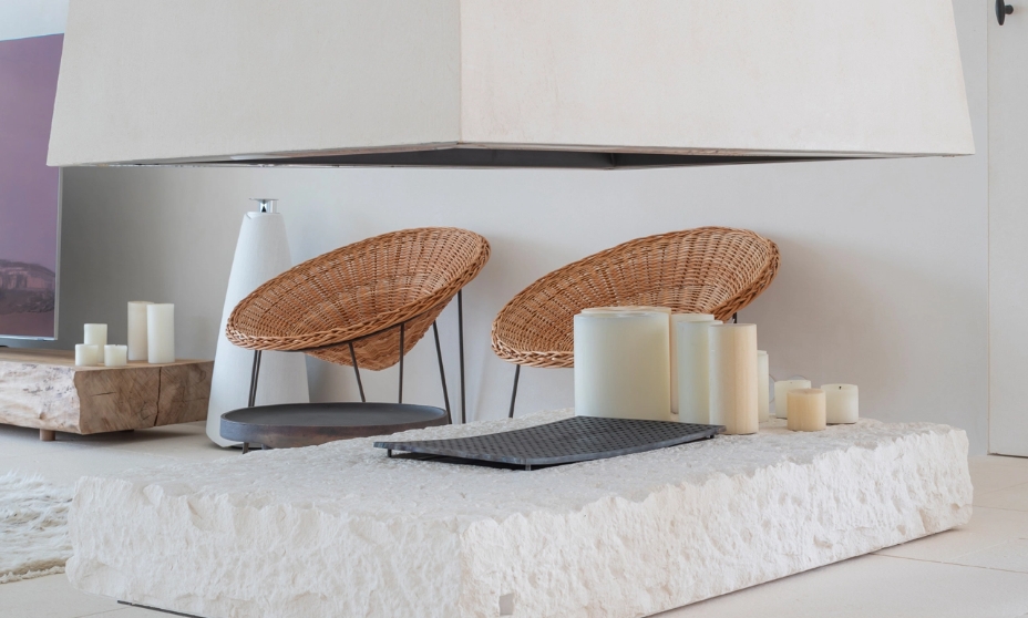 Minimalist fireplace suspended on a stone base with wicker armchairs and decorative candles.
