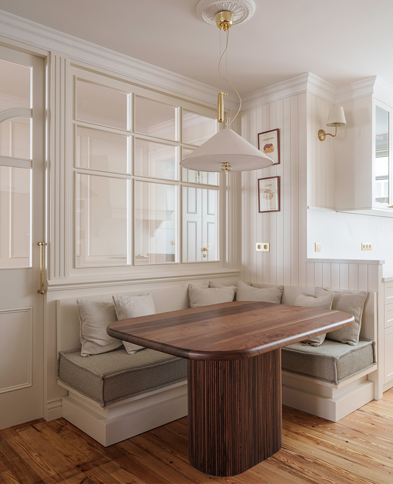 Comedor con mesa de madera, bancos integrados, cojines decorativos y una elegante lámpara colgante muy acogedora.