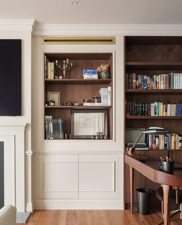 Estantería de madera oscura integrada en la pared con libros, objetos decorativos y una zona escritorio.