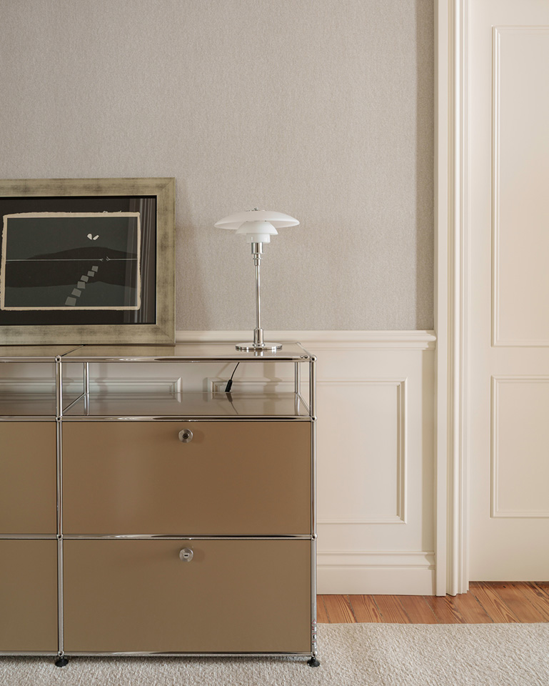 Mueble de almacenamiento color beige con cajones, una lámpara de mesa pequeña y un cuadro elegante.