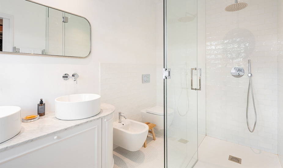 Baño moderno con diseño en color blanco, equipado con lavabos, bidé y ducha de cristal.