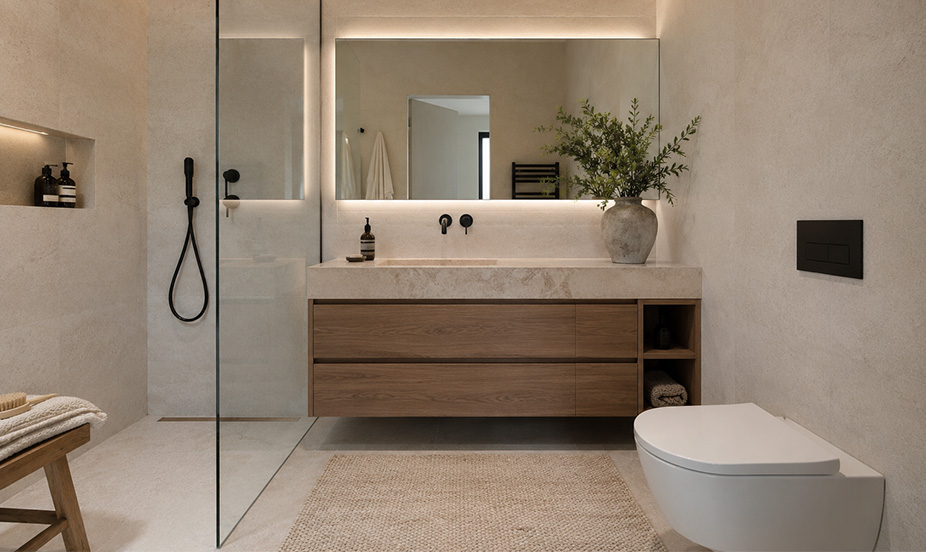 Baño moderno con tonos neutros, muebles de madera, espejo iluminado, ducha acristalada y elegante decoración minimalista.