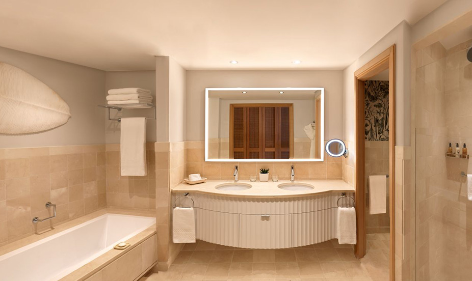 Baño espacioso que cuenta con doble lavabo y un gran espejo moderno retroiluminado muy brillante.