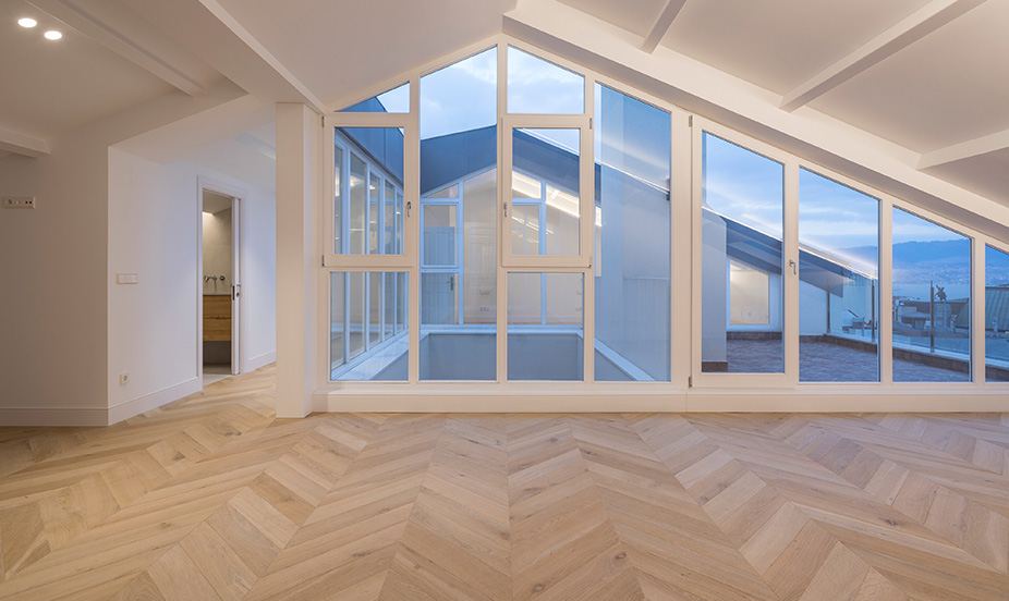 Spacious, bright living room with herringbone wood flooring and large windows with exterior views