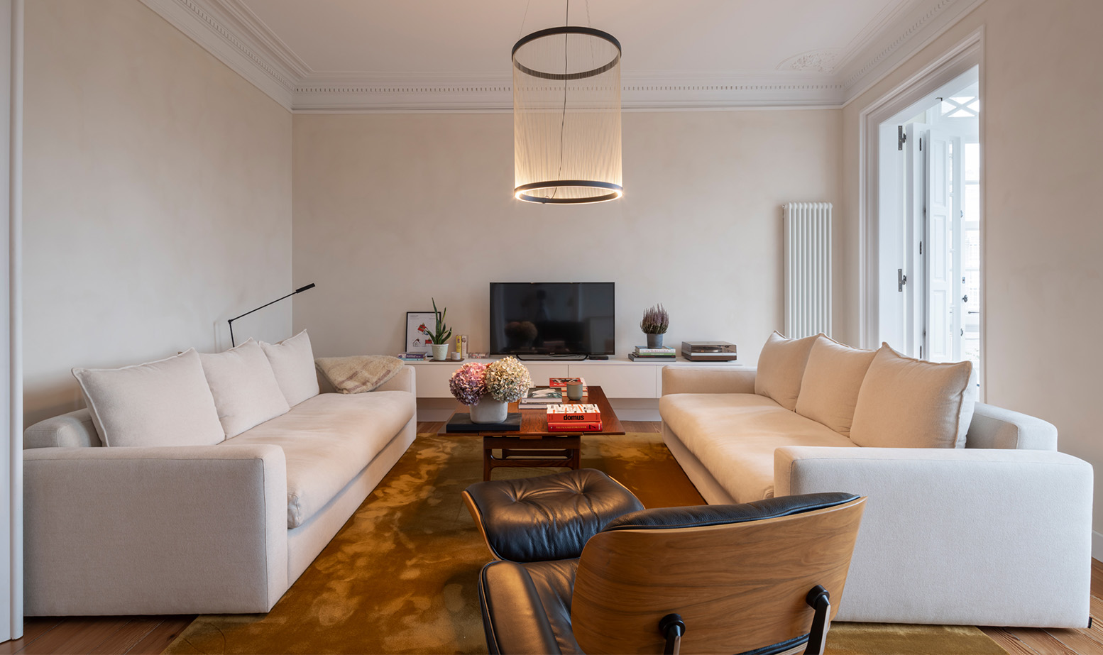 An elegant living room with two beige sofas facing each other, a mustard-colored rug, and a modern pendant light.