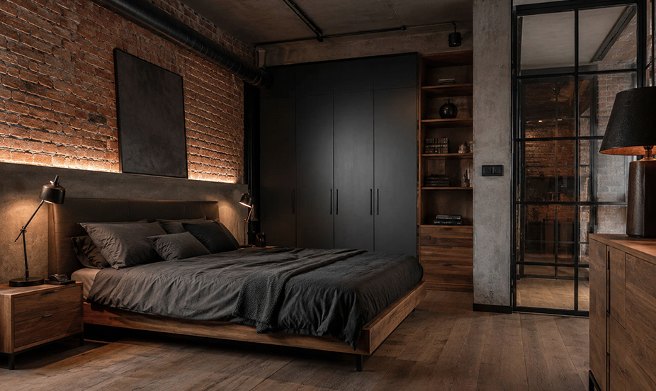 A bedroom with exposed brick walls, soft lighting, a metal frame, and dark materials that lend it great character.