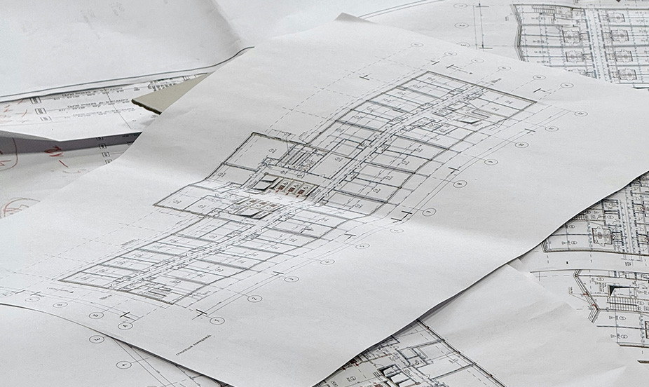 Several architectural blueprints with detailed technical drawings laid out on a work table.