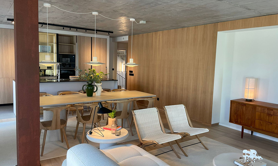 Espacioso salón comedor moderno con paredes de madera, lámparas suspendidas, mobiliario acogedor y detalles con plantas verdes.
