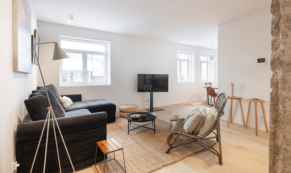A minimalist room with a dark sofa, a jute rug, a TV in the center, and a classic chair.