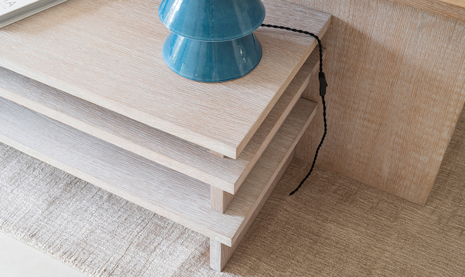 Detalle de mueble de madera clara junto a alfombra vegetal y una lámpara cerámica de tono azul.