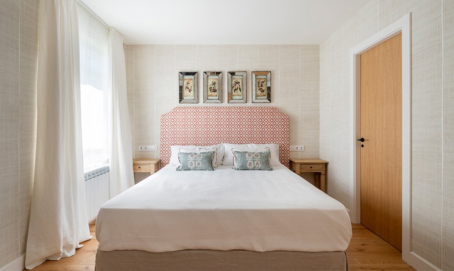 Dormitorio luminoso con tonos claros, cabecero estampado, textiles blancos, madera natural, distribución ordenada, ambiente sereno y acogedor elegante.