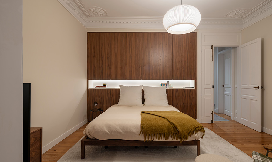 Dormitorio minimalista con mobiliario nogal, iluminación integrada, textiles suaves, molduras clásicas, líneas limpias, equilibrio, sofisticación y calidez.