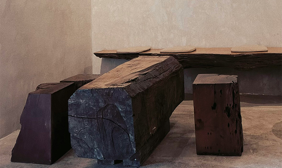 A solid-wood bench and stools—dark and rustic—against a beige stucco wall.