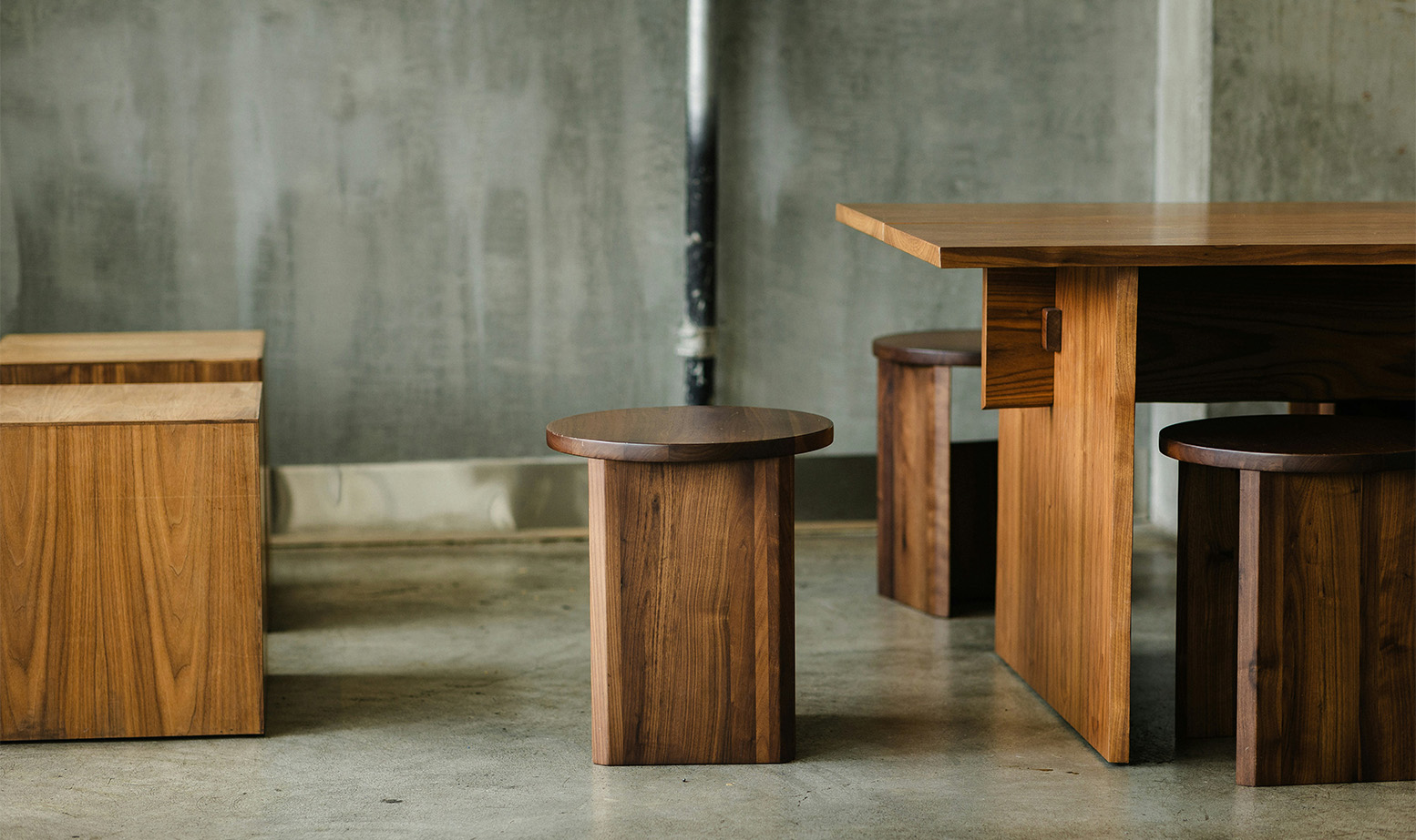 Modern furniture made of light and dark walnut wood, featuring square tables and round stools.