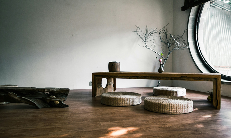 A minimalist Zen-style dining room with wooden floors, jute cushions, and a round window.