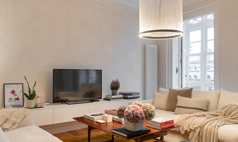 Sofá claro con cojines decorativos, manta de punto, mesa madera, flores secas, luz natural y ambiente acogedor elegante.
