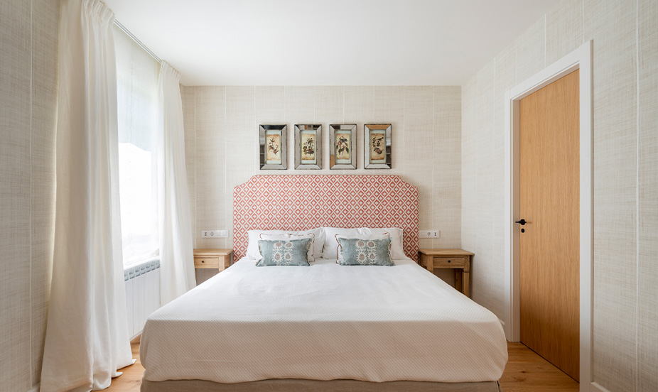 A bedroom decorated in neutral tones, featuring elegant ambient lighting that highlights the textiles and the headboard.