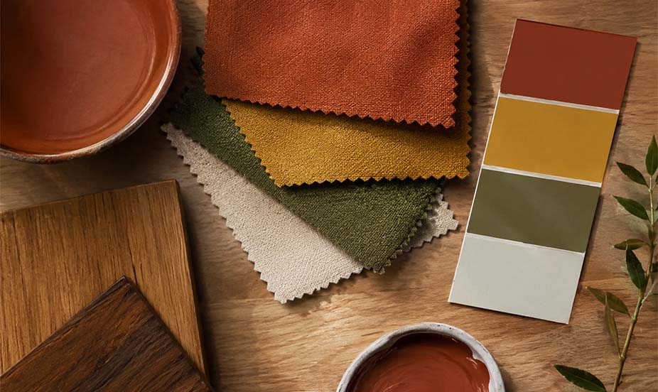 An autumnal color palette featuring colorful fabric swatches, paint shades, natural wood, and a ceramic bowl on a table.