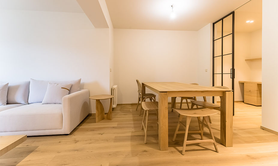 Comedor de madera conectado al salón y a la cocina mediante una moderna puerta corredera de cristal con marcos negros.