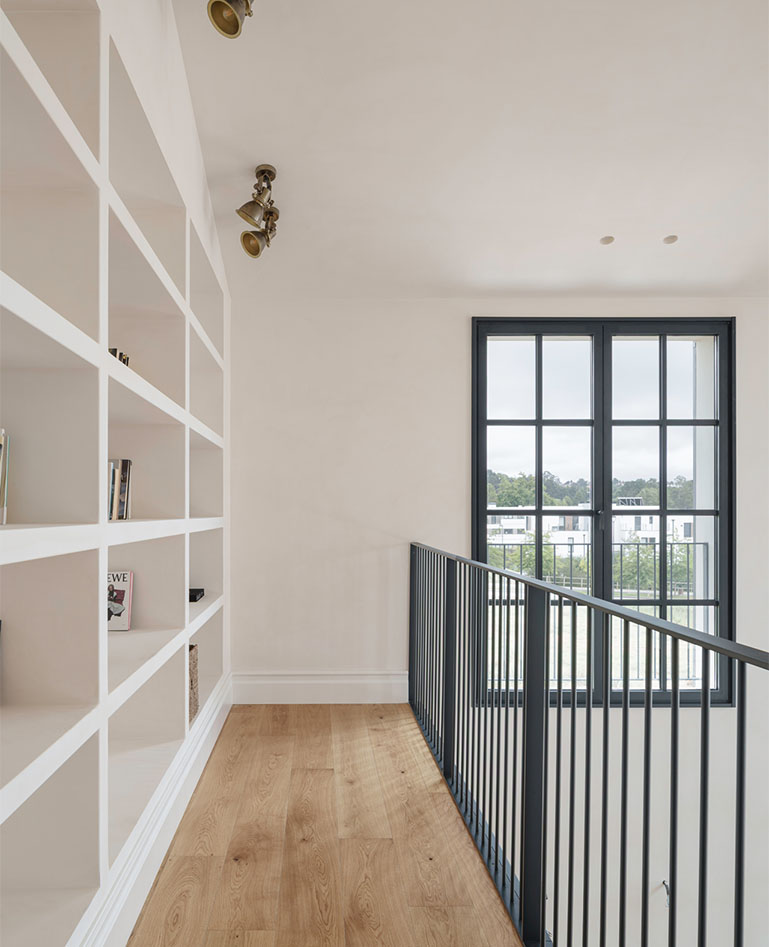 A custom-built white bookshelf built into the upper level of a home, featuring a metal railing and wooden flooring.