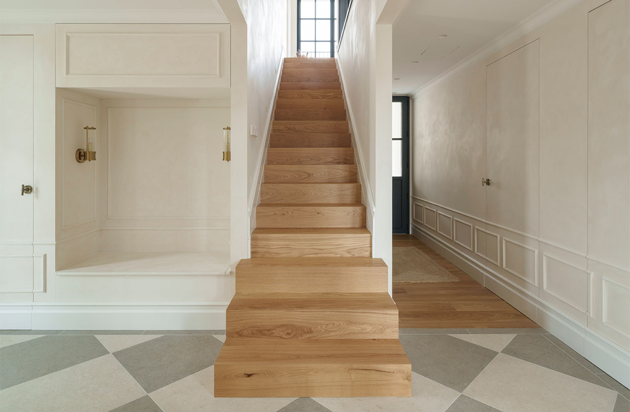 A custom-made oak staircase in the entryway of a home, featuring white decorative paneling and a geometric floor pattern.