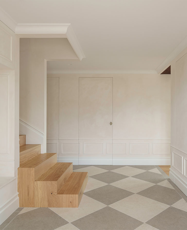 Entrance hall of a single-family home with an oak staircase, built-in doors, and white decorative moldings.