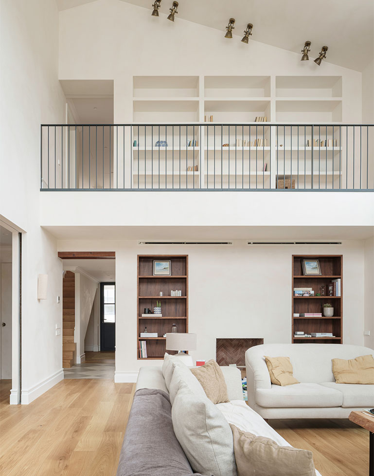 Double-height living room in a single-family home with custom built-in bookshelves, a metal railing, and hardwood floors.